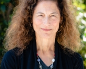 Head shot of Alexia Salvatierra. She is a professional looking woman with curly hair, a beaded necklace, and a knowing smile.